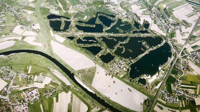 Aerial view of dark quarry lakes, river channel, patchwork farmland, small villages and green islands forming a scenic rural water landscape.