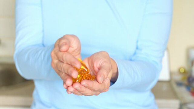 Unrecognizable woman holding pile of fish oil capsules on light background, closeup. Softgel omega 3 or D3 supplement capsules in female hands.