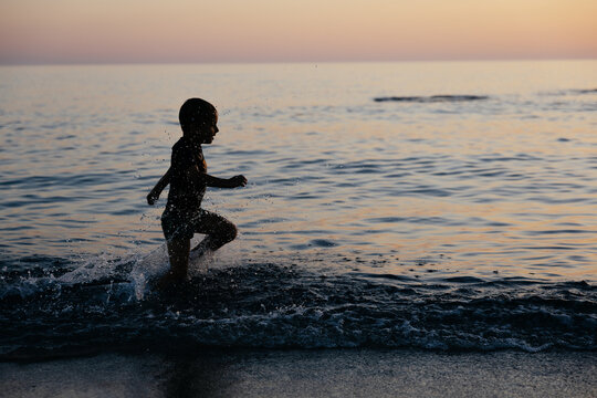 Silhouette of cute kids playing in water by the sea at sunset. 