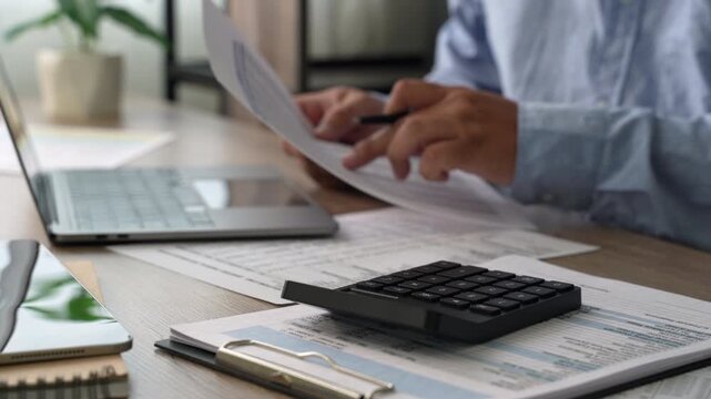 Corporate finance budgeting and accounting professional calculating financial documents with calculator and laptop in office