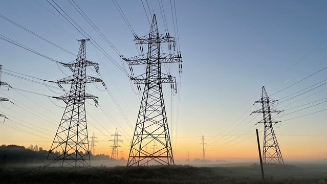 High voltage power transmission lines at sunrise with morning fog, electricity pylons across rural landscape, energy infrastructure, scenic industrial background