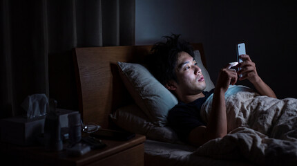 Fototapeta premium 真剣な表情でメッセージを確認する夜のベッドの男性 ｜ 緊張感ある視線