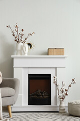 Fototapeta premium Stylish fireplace and vases with cotton flowers near white wall in interior of living room