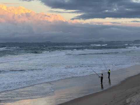 Fishermen casting lines into the ocean surf during a golden hour sunset