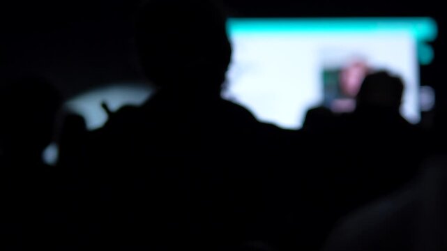Out of focus silhouettes of people attending a startup seminar or AI technology event in a dark auditorium.