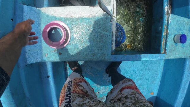 Close-up perspective of a local fisherman's hands expertly unhooking a catch while working on a traditional panga boat at sea.