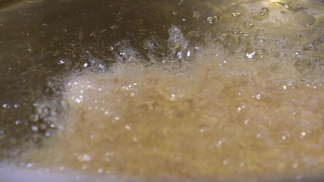 Detailed view of food being deep-fried in bubbling, hot, golden cooking oil in a pan