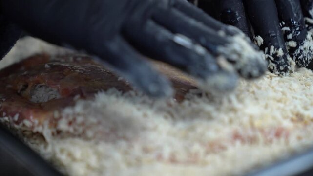 Professional chef in black gloves carefully breading raw meat fillets in panko crumbs