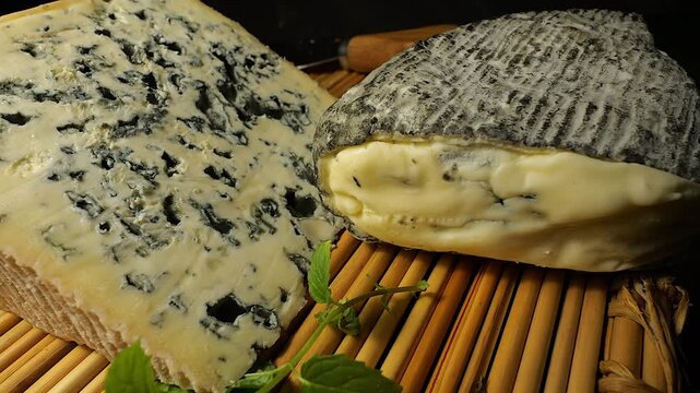 50p close up of Bleu d&rsquo;Auvergne and Roche Baron cheeses displayed on a bamboo mat. Gourmet French dairy products presented in warm studio lighting