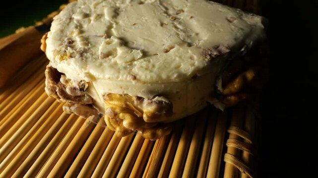 50p close up of an artisanal cheese wheel coated with walnuts on a bamboo mat. Gourmet dairy product filmed with warm light and shallow depth of field.