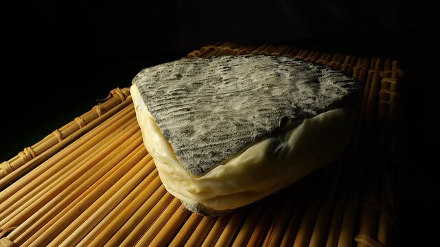 50p close up of Roche Baron cheese resting on a bamboo mat. French soft cheese with distinctive ash rind and creamy texture in warm studio lighting