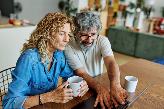 Portrait of a lovely senior mature couple using a laptop together and having fun drinking coffee or tea sitting at a table at home