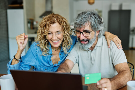 portrait of happy smiling senior elderly couple using a laptop computer and a credit card  for online shopping at home, technology and internet use in everyday life concept