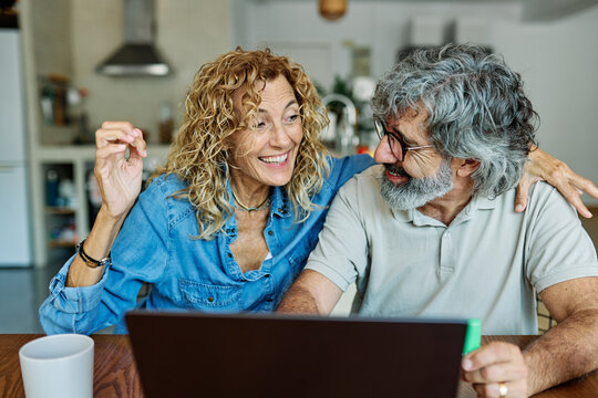 portrait of happy smiling senior elderly couple using a laptop computer and a credit card  for online shopping at home, technology and internet use in everyday life concept