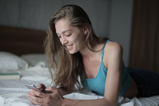 Happy young woman scrolling on her smartphone in bed