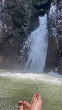 A peaceful travel and nature video featuring crystal-clear water flowing through a hidden mountain waterfall surrounded by rugged rocks and lush greenery. 
