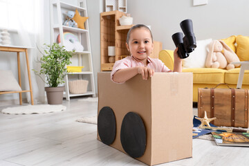 Obraz premium Cute little girl with binoculars in cardboard car at home