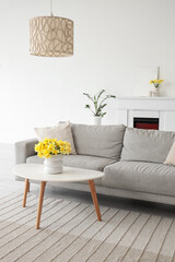 Fototapeta premium Interior of living room with grey sofa, fireplace and daffodils in vases