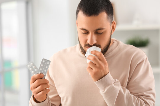 Sick young man with tissue and pills suffering from allergy at home