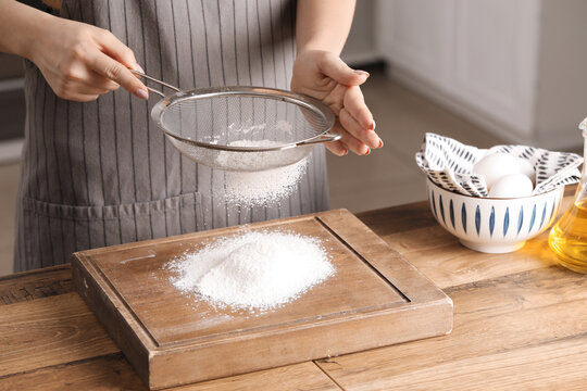 Woman with sieve sifting flour on table in kitchen