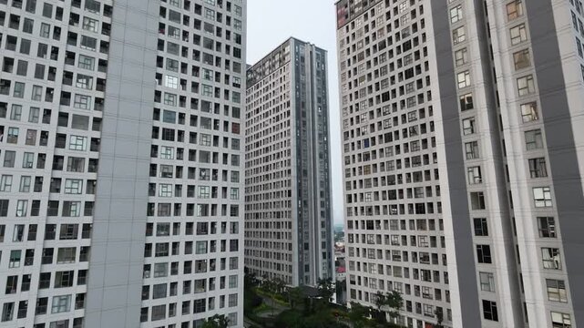 Aerial drone footage slowly descending between dense modern high-rise residential apartment buildings to reveal a large courtyard swimming pool