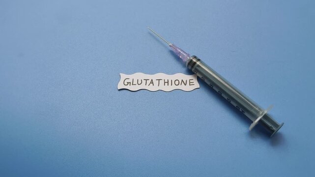 Syringe near glutathione word with copy space. Antioxidant medicine injection for skin whitening, anti-aging, oxidative stress reduction and dark spot pigmentation treatment. Close up top view.