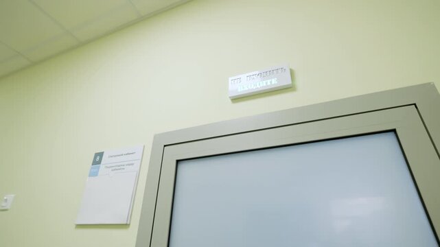 Modern clinic corridor displays digital cue panel with Cyrillic text over office entrance. Bright ceiling lights create pristine atmosphere