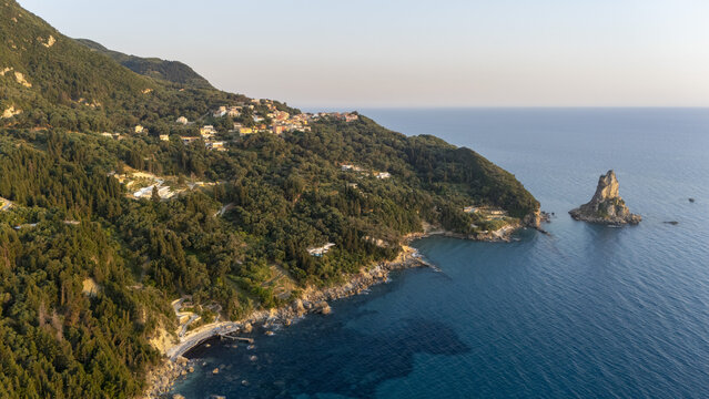 Aerial view of the rugged coastline and Paralia Fieroulas with lush green hills, dense Mediterranean vegetation, and a sea stack rising from the clear blue Ionian Sea in Greece.