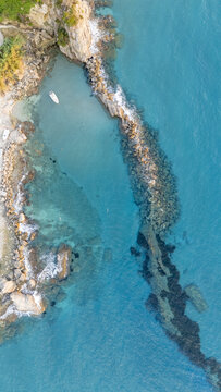 Aerial view of Paralia Fieroulas featuring a small rocky cove with turquoise water, a stone breakwater, and a small boat moored near the shore in Greece.