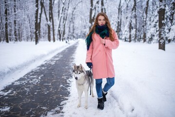 Red-haired girl walking with a husky dog on a snowy park path © Nomad_Soul