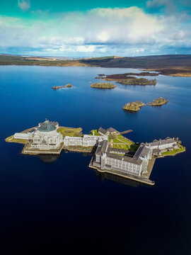 Aerial view of St Patrick's Purgatory on Station Island in Lough Derg, surrounded by deep blue water and rolling green hills under a cloudy sky, County Donegal, Ireland.