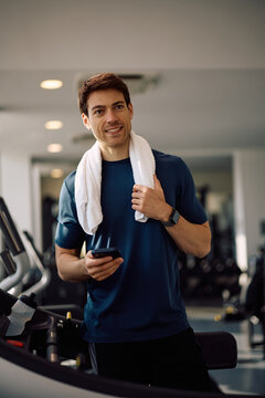 Happy athletic man using app on cell phone during sports training in health club.