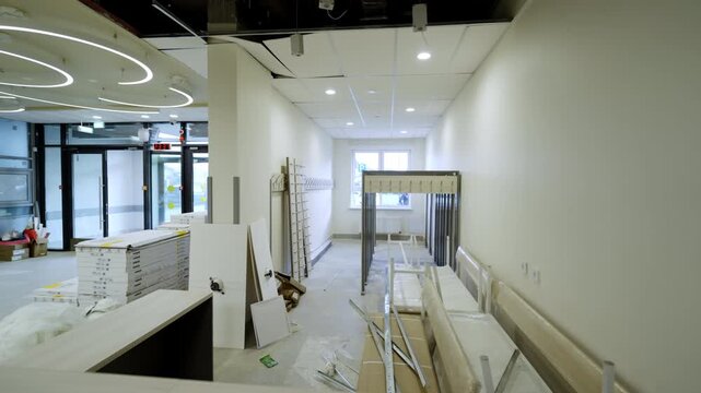 Unfinished school locker room features stacked panels and plastic wrapped benches. Spotlights illuminate empty under-construction space
