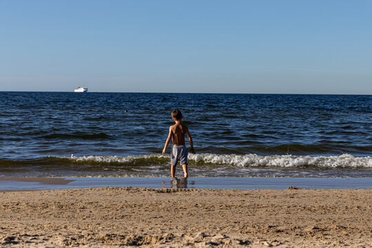 A boy on a sandy beach looks at the waves of the Baltic Sea, view from the back. Herinsdorf, Germany