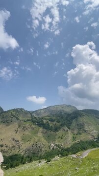 Vertical nature footage captured at Malsa, Abbottabad, Pakistan, showcasing rugged mountain cliffs, lush green hills, dramatic white clouds, and a breathtaking blue sky. Ideal for travel videos, 