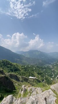 Vertical nature footage captured at Malsa, Abbottabad, Pakistan, showcasing rugged mountain cliffs, lush green hills, dramatic white clouds, and a breathtaking blue sky. Ideal for travel videos, 