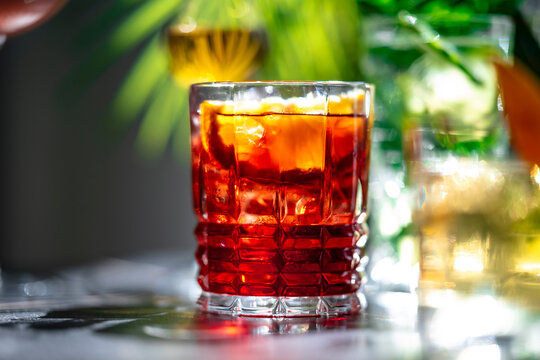 Cold summer cocktails menu includes alcoholic drinks like ruby red Negroni with orange peel garnish. Timeless Italian aperitif, dark bar counter, moody night shadows, luxury hospitality concept.