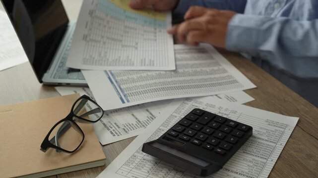 man use calculator while holding a financial document beside a laptop, showing budgeting, accounting, and report review workflow for corporate finance planning process.