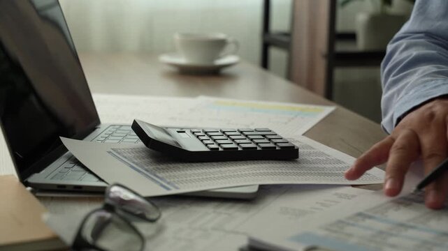 man use calculator while holding a financial document beside a laptop, showing budgeting, accounting, and report review workflow for corporate finance planning process.