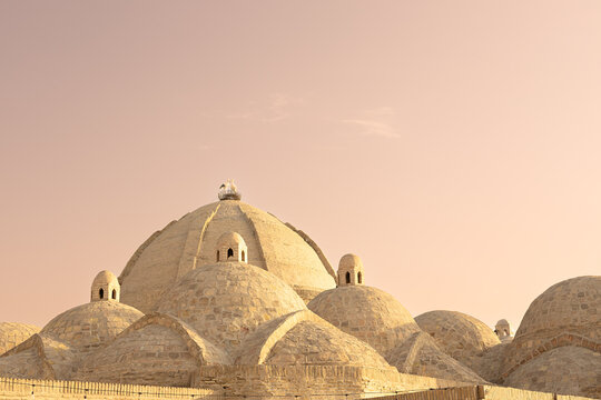Domed rooftops of Toqi Zargaron bazaar in Bukhara with a stork nest on the central dome. Historic brick architecture bathed in warm sunset light, ideal for travel and heritage publications.