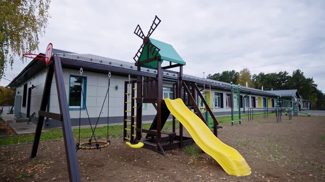 Small basketball hoop and children swings look cheerful near long facility. Quiet outdoor space feels peaceful under cloudy autumn sky