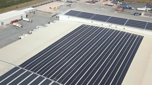 Massive solar panel arrays cover a cold storage warehouse roof while semitrailers position around the surrounding truck yard.