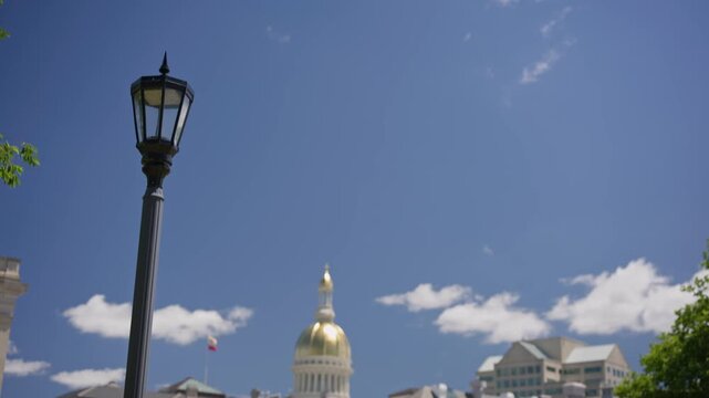 Cinematic tilt up view of the New Jersey State House capitol building framed by a historic lightpost in downtown Trenton New Jersey on a bright day.