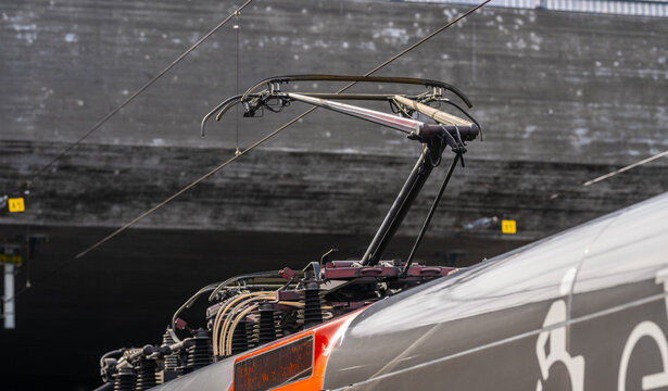 Close up of electric train pantograph connecting to overhead power lines in railway station.