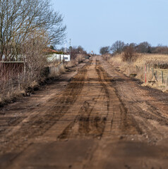 Fototapeta premium Muddy rural dirt road stretching through dry grass landscape with distant horizon Nature.