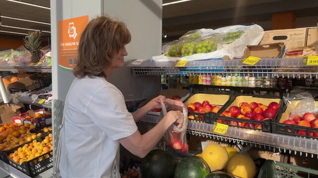 A happy 66-year-old woman shopping in a hypermarket, selecting fresh fruits and vegetables. Healthy eating and a healthy lifestyle in later life.