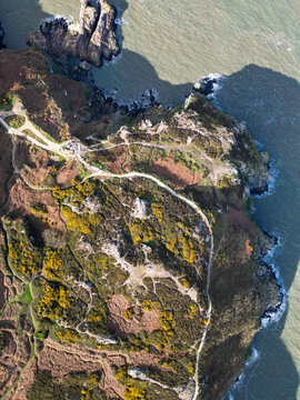 Aerial view of the rugged cliffs and coastal trails of Howth, featuring yellow gorse bushes, rocky terrain, and the sea meeting the coastline in Dublin, County Dublin, Ireland.