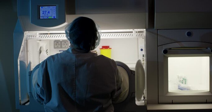 Rear view of scientist operating equipment inside laboratory workstation with glowing window