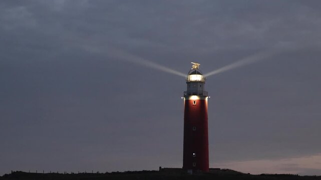Red Lighthouse with Rotating Light Beam at Dusk on the Coast of Texel, Netherlands