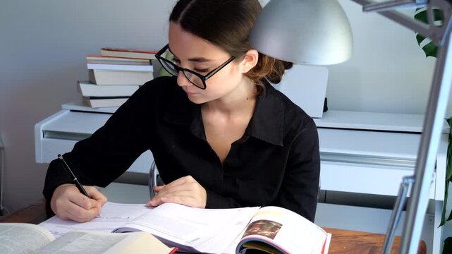 50p close up shot of a teenage student writing notes while studying at a desk with books and educational materials in a home learning environment